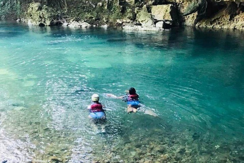 Dos personas nadando en aguas claras, con terreno rocoso al fondo. 3