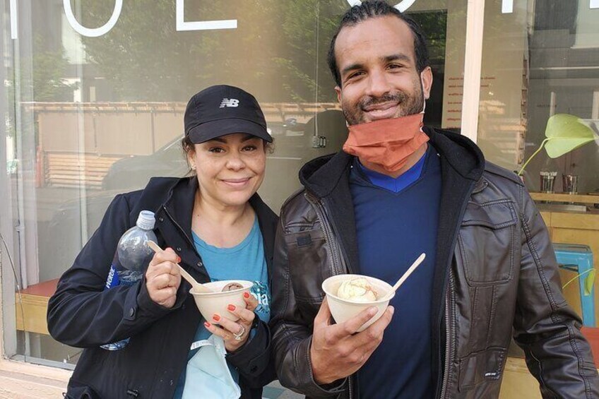 Two people holding bowls of food in front of a storefront. 3