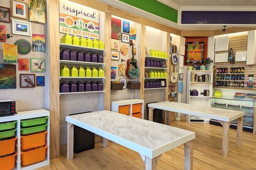 An art studio with tables, shelves of art supplies, and various artworks on display. 2