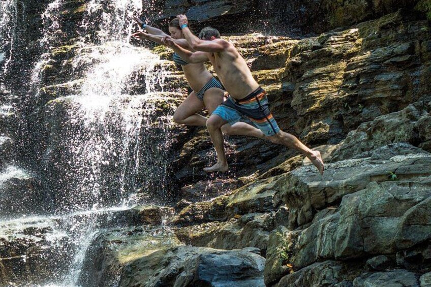 Twee personen springen van een rotsklif in een waterval. 1