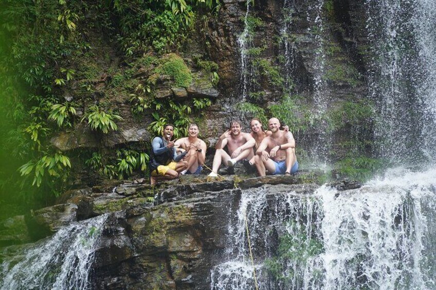 Un grupo de personas sentadas en un saliente rocoso junto a una cascada. 3