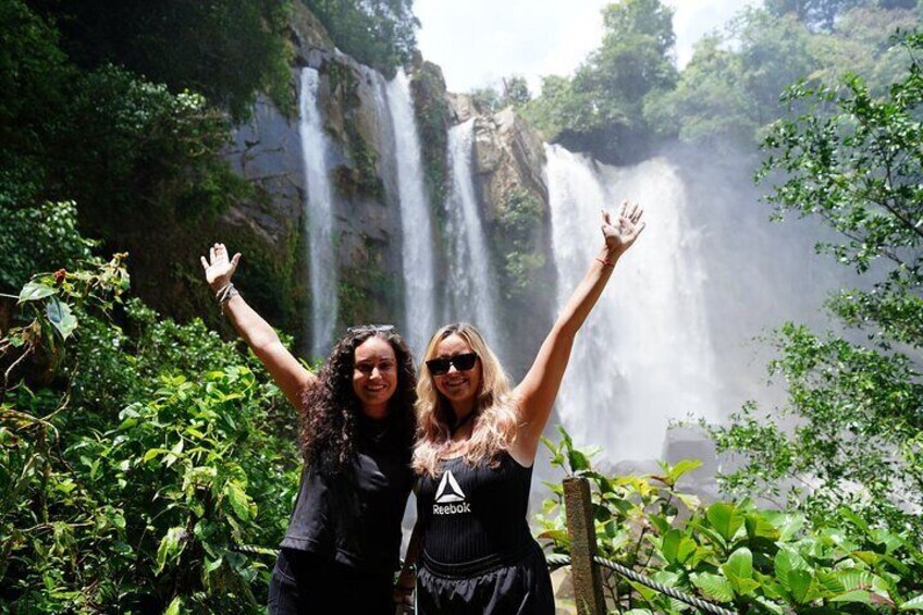 Dos personas de pie frente a una cascada, con los brazos levantados. 5