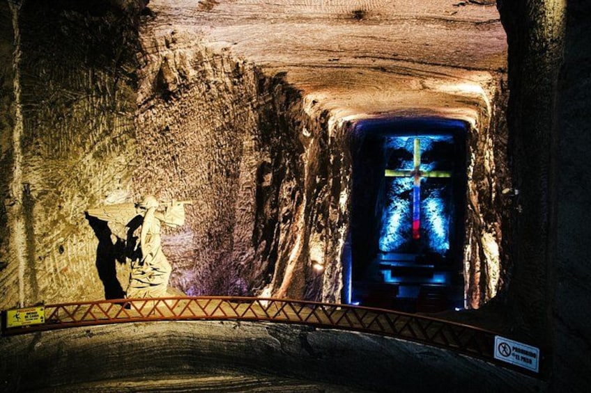 A cave with a cross at the end of a tunnel and a person standing near the entrance. 1