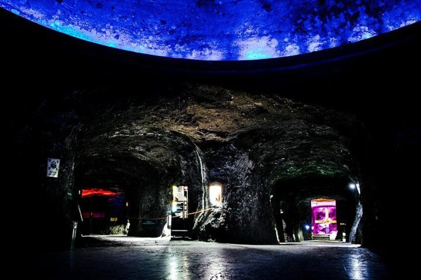 An underground tunnel with graffiti on the walls and a neon sign in the distance. 2