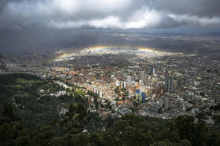 Stadtansicht mit Regenbogen, dicht bebautem Stadtgebiet und umgebender Grünfläche. 2