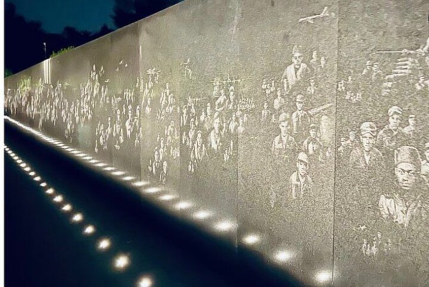 A long wall with engraved figures of people, illuminated by lights. 5