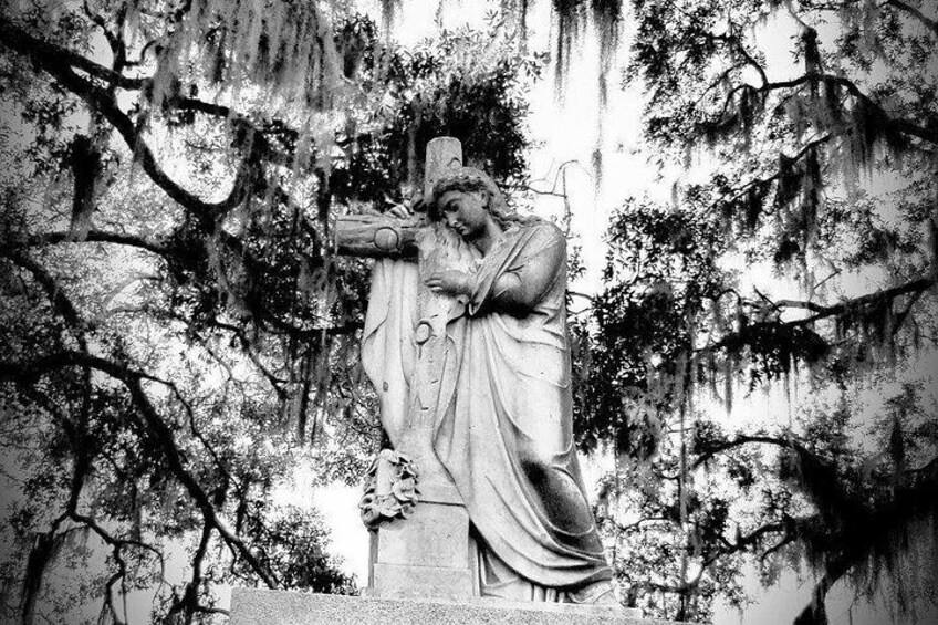 A statue of a man holding a cross, surrounded by trees and moss. 5