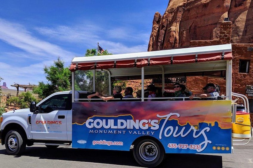 Un autobús turístico con la marca 'Goulding's Monument Valley Tours' estacionado frente a un paisaje rocoso. 1