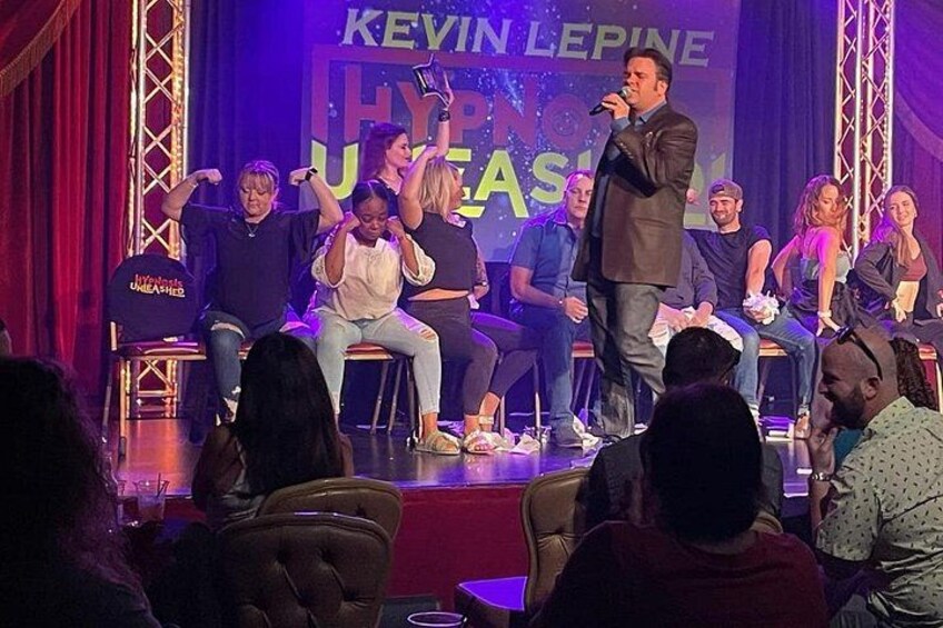 Un escenario con un soporte para micrófono, un público sentado y un cartel con texto. 3