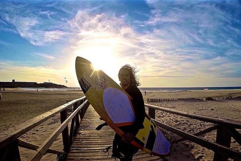 A person holding a surfboard on a wooden boardwalk with the ocean in the background. 1
