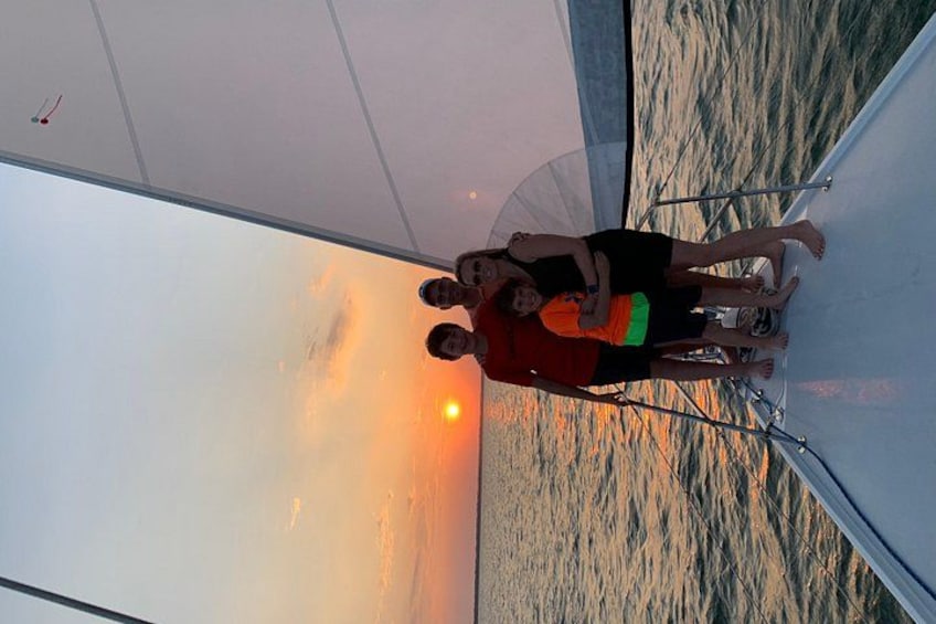 Solnedgang over vand med sejlbåd og mennesker på dækket. 2