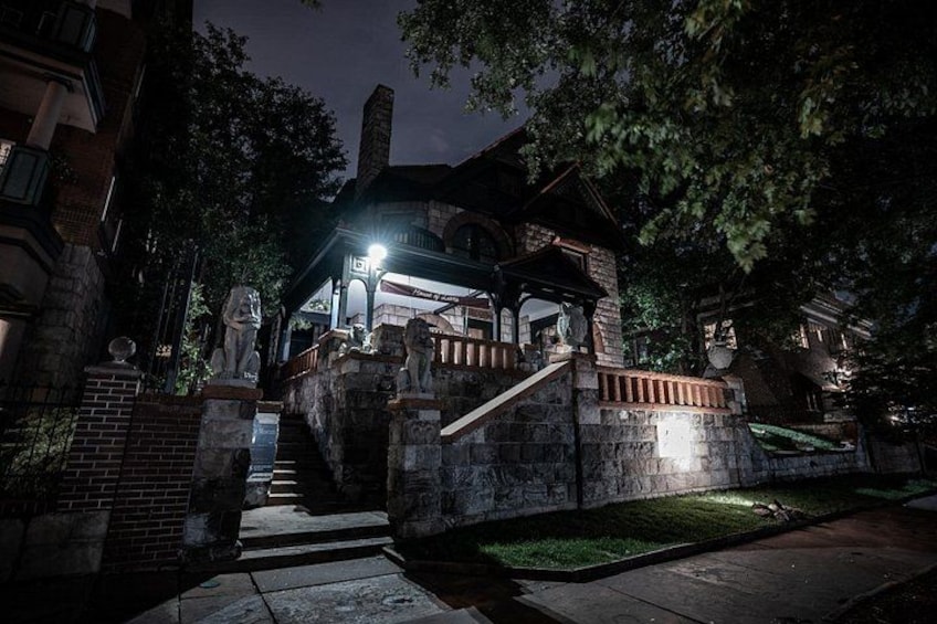 A historic house with a stone staircase, a porch, and a well-lit front door. 2