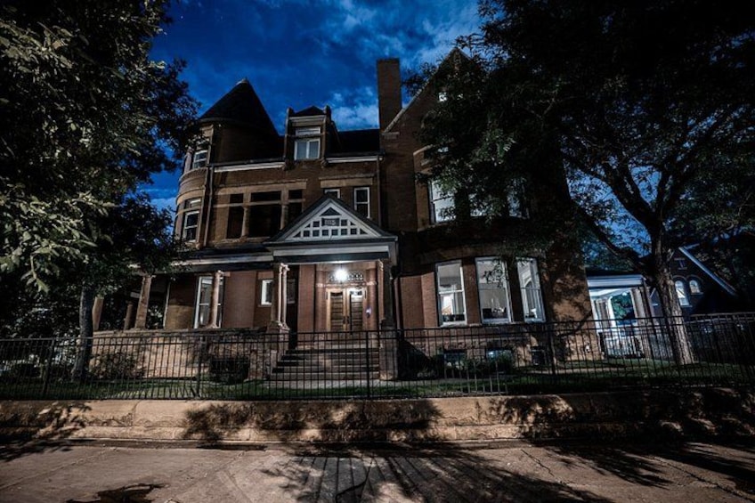 A large, historic brick house with a prominent front porch and a well-maintained lawn. 3