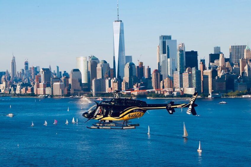 En helikopter flyger över en sjö med segelbåtar, och i bakgrunden syns en stads silhuett. 4