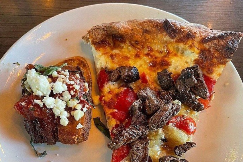 En tallerken med et pizzastykke med ost, røde peberfrugter og svampe, samt en bruschetta med tomater, ost og krydderurter. 2