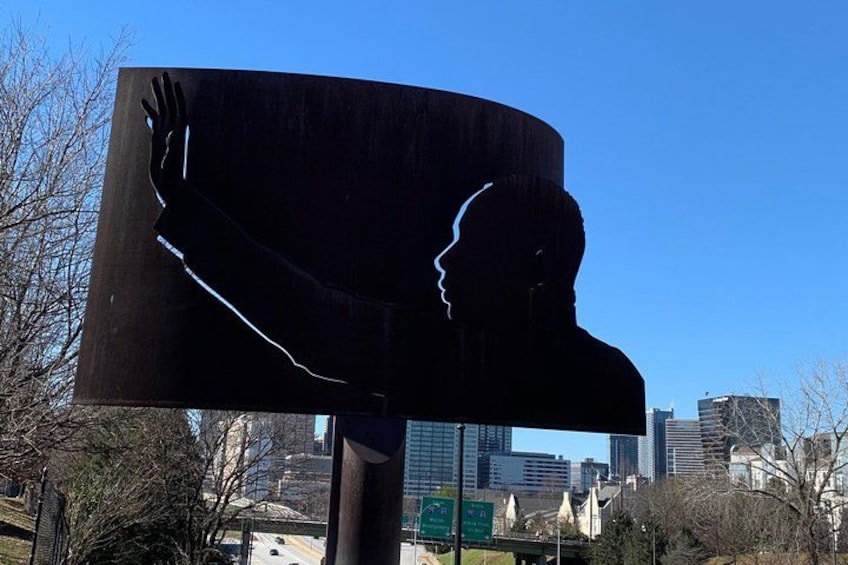 A large metal sculpture of a human profile with a hand, set against a city skyline. 3
