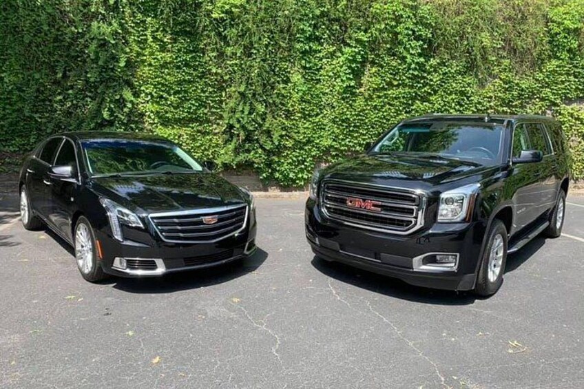 Two black GMC SUVs parked in a lot with a green hedge in the background. 2