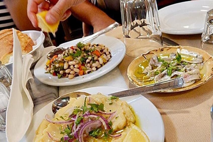 A table with various dishes, including a salad with beans and vegetables, a seafood dish with lemon, and a plate with a creamy dish garnished with herbs. 1