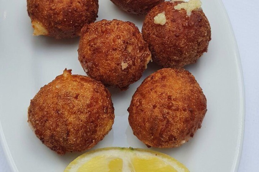 A plate of golden-brown fried balls with a lemon wedge. 2