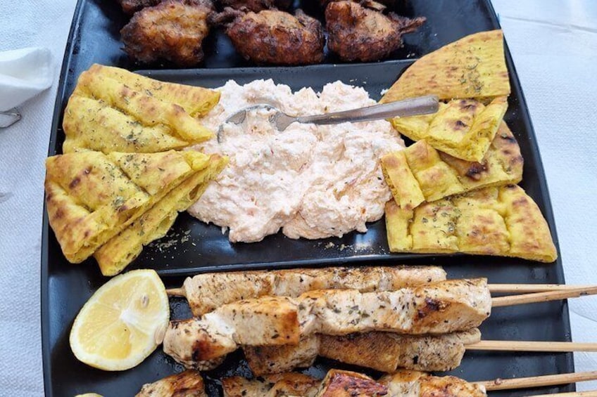 A variety of grilled meats, flatbreads, and a creamy dip on a black tray. 4