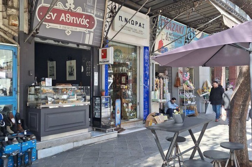 A street with shops, a coffee stand, and a person sitting on a bench. 3