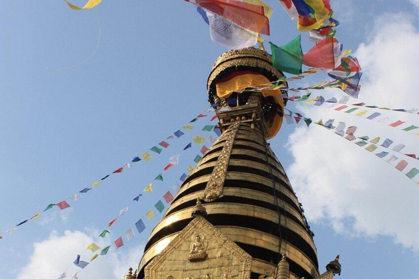 A tall, striped tower with a golden top, adorned with colorful prayer flags. 2