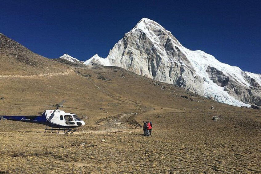 A helicopter parked on a barren landscape with a snow-capped mountain in the background. 1