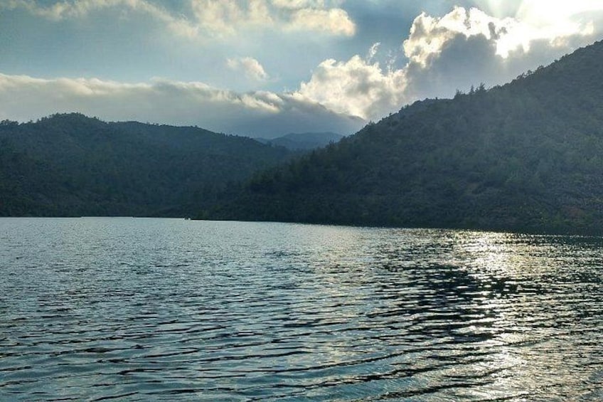 A calm lake with reflections of the sky, surrounded by forested hills. 3