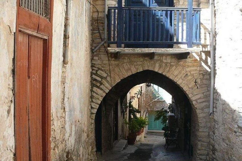 A narrow stone archway, a wooden door, and a balcony with blue railings. 1