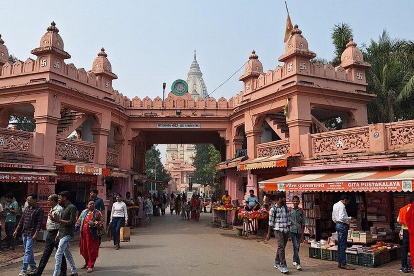 A bustling market with pink arches, people walking, and a temple in the background. 2