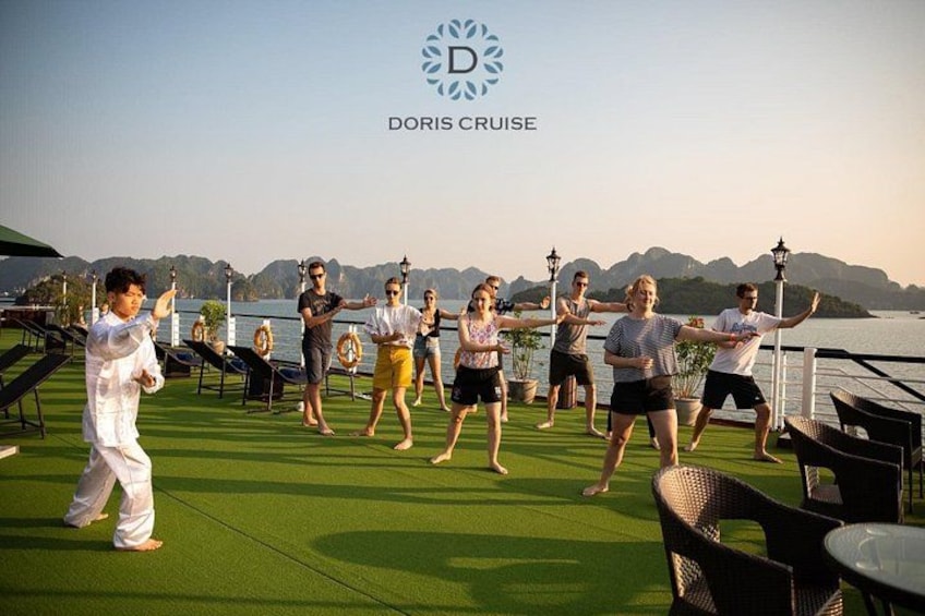 A group of people performing a synchronized dance on a deck with a scenic view of mountains and water in the background. 4