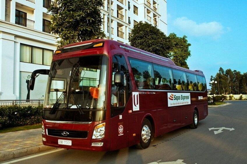 Un autobús rojo de Sapa Express estacionado en una carretera con un edificio al fondo. 2