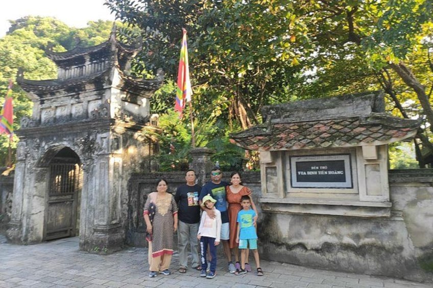 A family posing in front of an ancient gate with a plaque, surrounded by trees and flags. 4