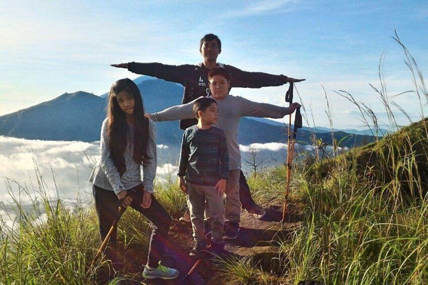 A family on a mountain trail with a view of clouds below and a mountain in the background. 2