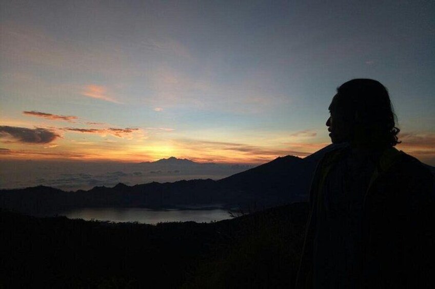 A silhouette of a person against a sunset with mountains and a lake in the background. 3