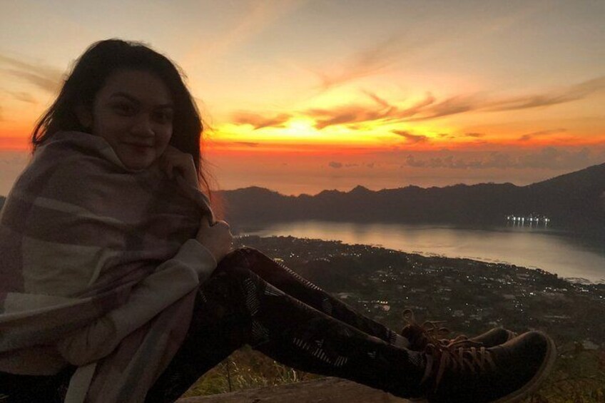 A person sitting on a hill overlooking a lake with a sunset in the background. 4