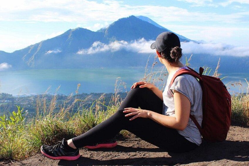 A person sitting on a rock with a backpack, overlooking a lake and mountains. 2