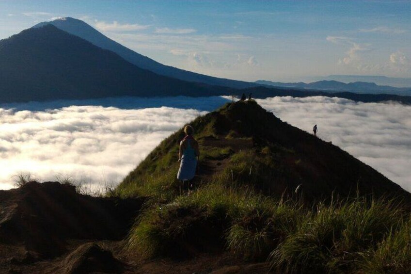 A person standing on a grassy hill overlooking a sea of clouds with a mountain in the background. 5