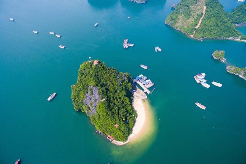 An aerial view of a lush green island surrounded by turquoise waters with several boats anchored near the shore. 3