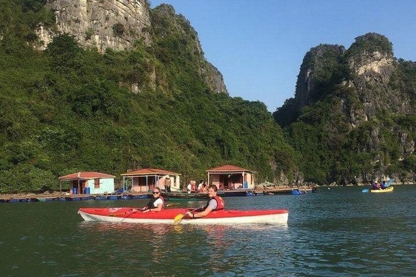Un kayak rosso su acqua calma, una casetta con tetto rosso e una grande formazione rocciosa sullo sfondo. 3