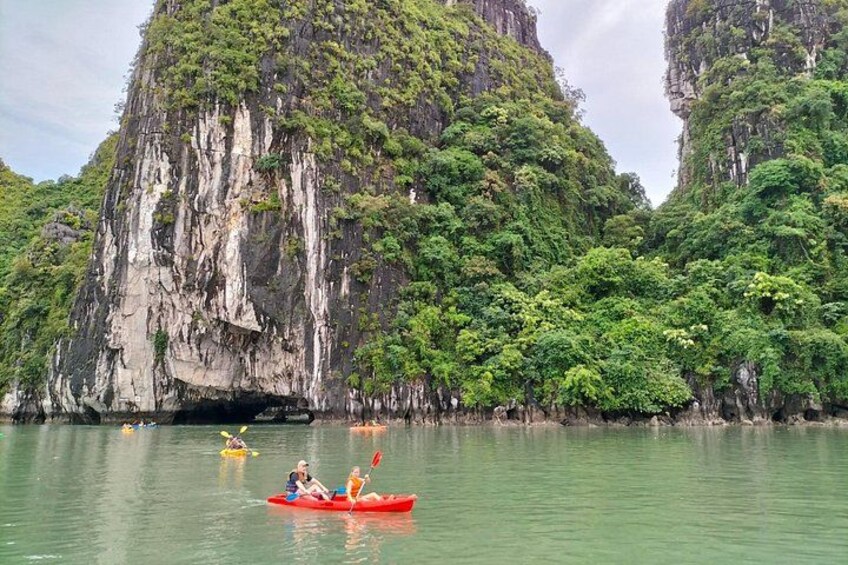 Un kayakiste dans un kayak rouge, sur une eau calme, entouré de falaises verdoyantes. 5