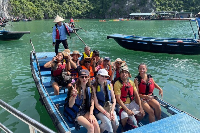 A group of people on a blue boat, wearing life jackets, on a calm river surrounded by greenery and other boats. 2