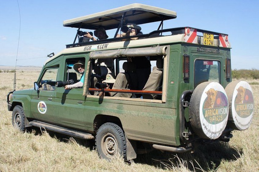 A safari vehicle with passengers, a license plate, and two large tires. 1