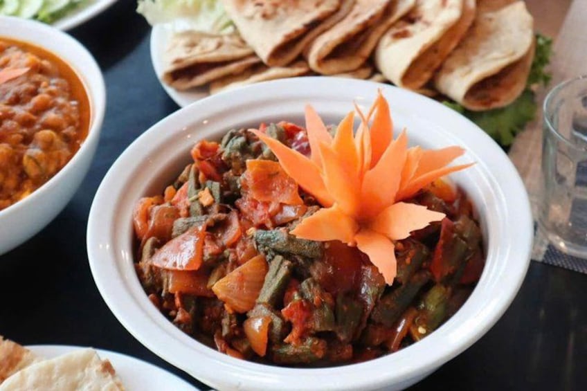 Un tazón de estofado de verduras adornado con flores de zanahoria, acompañado de pan plano y un guarnición. 4