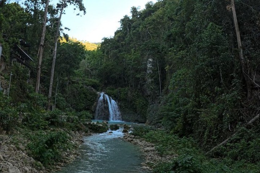 Une cascade située dans une zone boisée, caractérisée par une végétation luxuriante, avec une rivière qui la traverse. 5