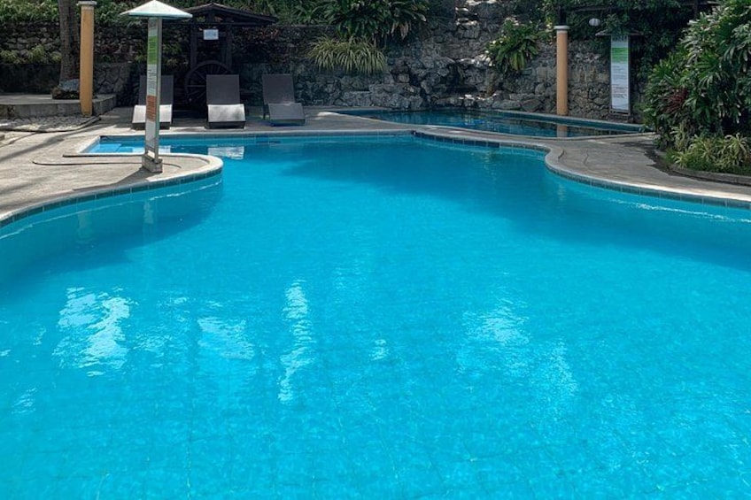 A clear blue swimming pool with lounge chairs and a stone wall in the background. 4