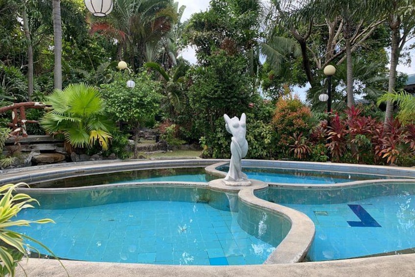A swimming pool with a statue, surrounded by lush greenery and palm trees. 5
