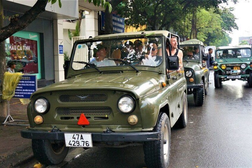 Ein militärähnliches Fahrzeug mit Kennzeichen, Passagiere und im Hintergrund ein weiteres, ähnliches Fahrzeug. 3