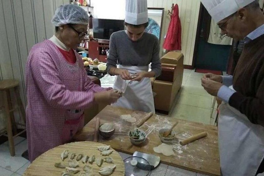 Three people in a kitchen preparing food, with dough on the table and kitchen utensils. 4