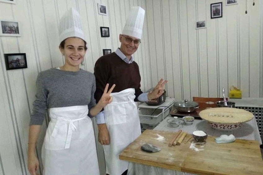 Two people in chef hats and aprons standing in a kitchen with a wooden table, a rolling pin, and a pie in the background. 5